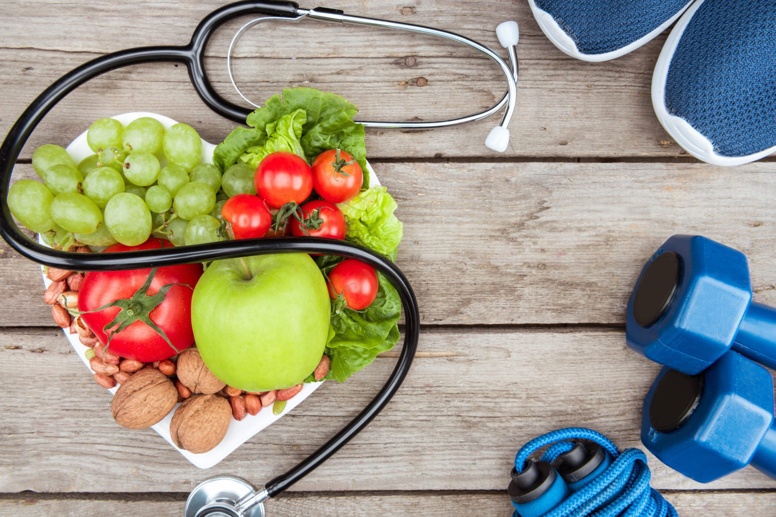 top view of stethoscope, organic vegetables and fruits and sport equipment on wooden surface,